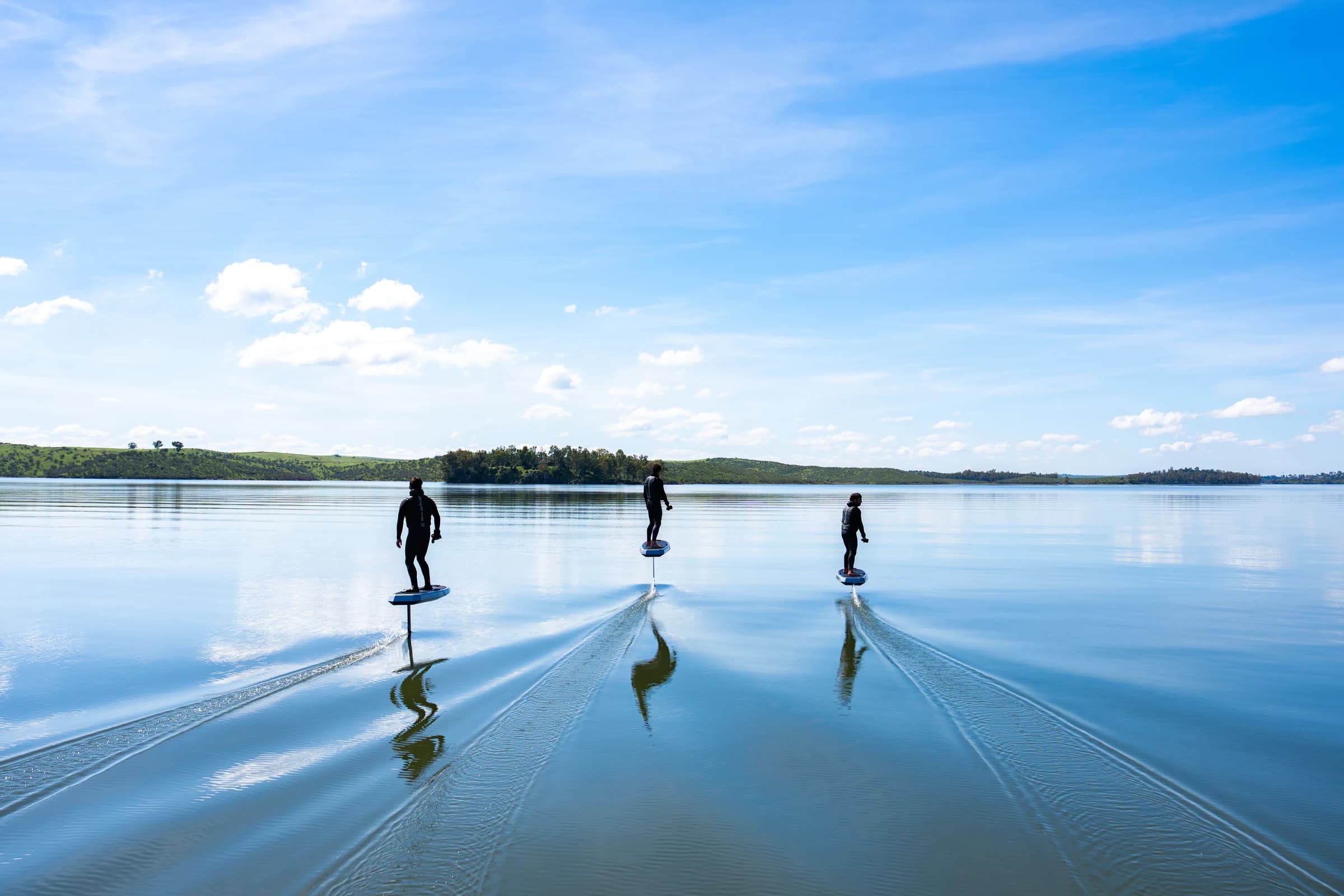 Three riders gliding across glassy water on Awake VINGA Carve electric hydrofoils